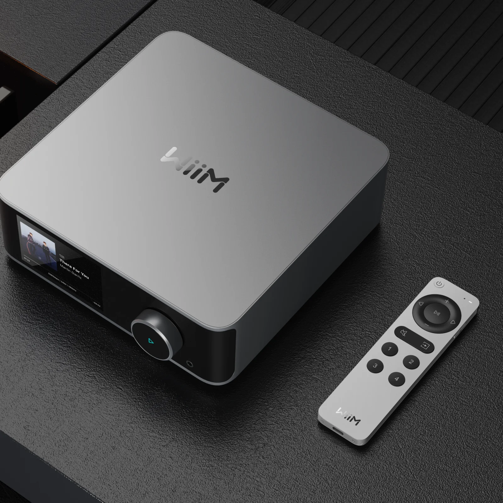 Voice Remote 2 à côté d’un streamer WiiM à écran sur un meuble sombre